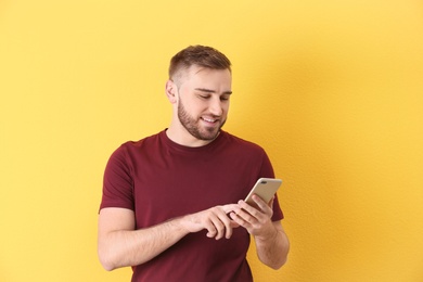 Photo of Portrait of smiling young man with mobile phone on color background