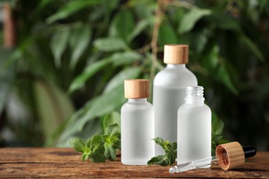 Photo of Bottle of mint essential oil and fresh leaves on wooden table against blurred background, space for text