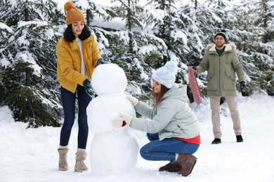 Photo of Happy people making snowman together outdoors. Winter vacation