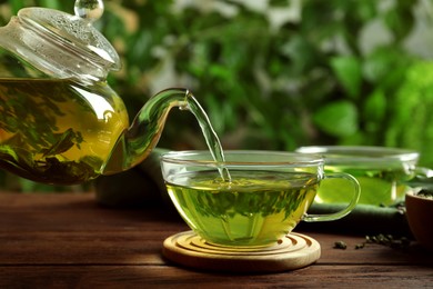 Photo of Pouring green tea into glass cup on wooden table