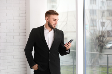 Photo of Young businessman using smartphone near window at home