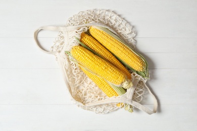 Photo of Bag of corn cobs on white wooden table, top view