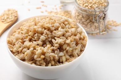 Photo of Delicious pearl barley in bowl on white tiled table, closeup