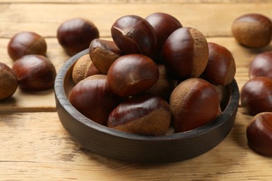 Photo of Sweet fresh edible chestnuts in bowl on wooden table, closeup