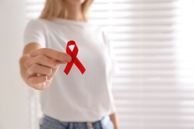 Photo of Woman holding red awareness ribbon on light background, closeup with space for text. World AIDS disease day