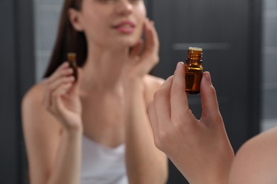 Photo of Young woman applying essential oil onto face indoors, closeup