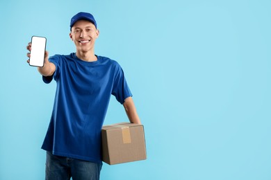 Photo of Happy courier with parcel and smartphone on light blue background. Space for text