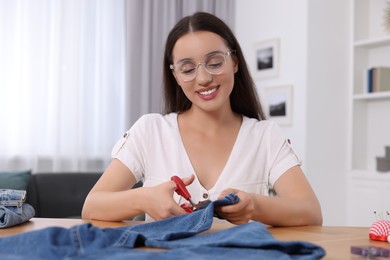 Photo of Happy woman cutting hem of jeans at table indoors