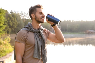 Photo of Young man drinking water on shore of beautiful lake. Camping season