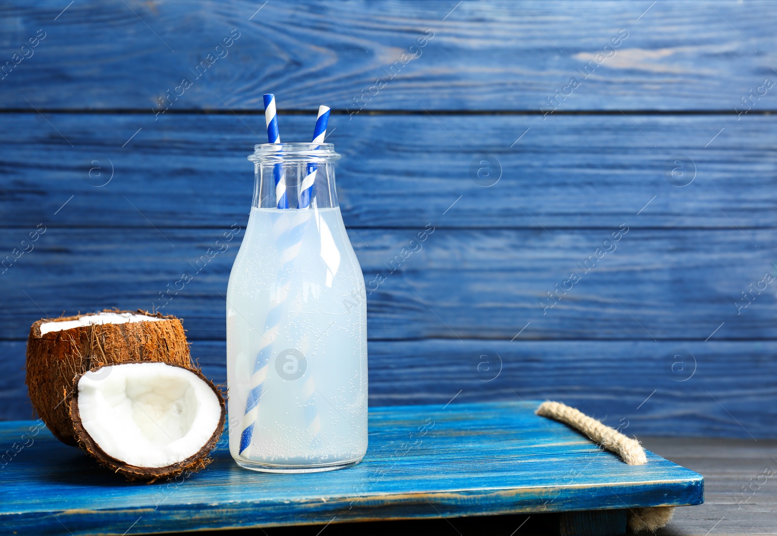 Photo of Bottle of coconut water with fresh nuts on wooden tray