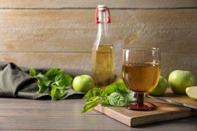 Photo of Delicious cider and apples with green leaves on wooden table, space for text