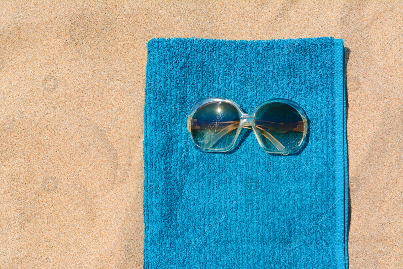 Photo of Soft blue beach towel with sunglasses on sand, top view. Space for text