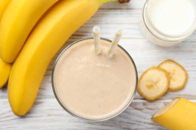 Photo of Glass of tasty banana smoothie with straws and ingredients on white wooden table, flat lay