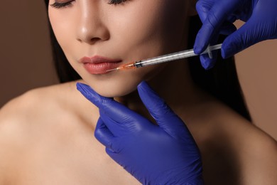 Photo of Woman getting lip injection on brown background, closeup