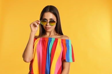 Photo of Beautiful young woman wearing sunglasses on yellow background