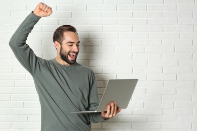Photo of Emotional young man with laptop celebrating victory near brick wall. Space for text