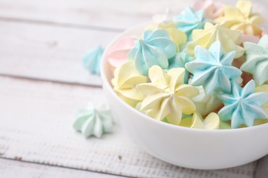 Photo of Tasty meringue cookies in bowl on white wooden table, closeup. Space for text