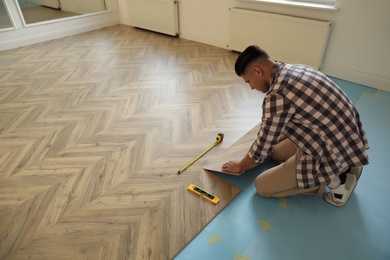 Photo of Professional worker installing new parquet flooring indoors