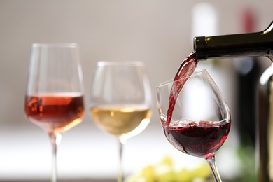 Photo of Pouring red wine from bottle into glass on blurred background. Space for text
