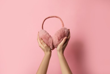 Photo of Woman holding stylish winter earmuffs on pink background, closeup. Space for text