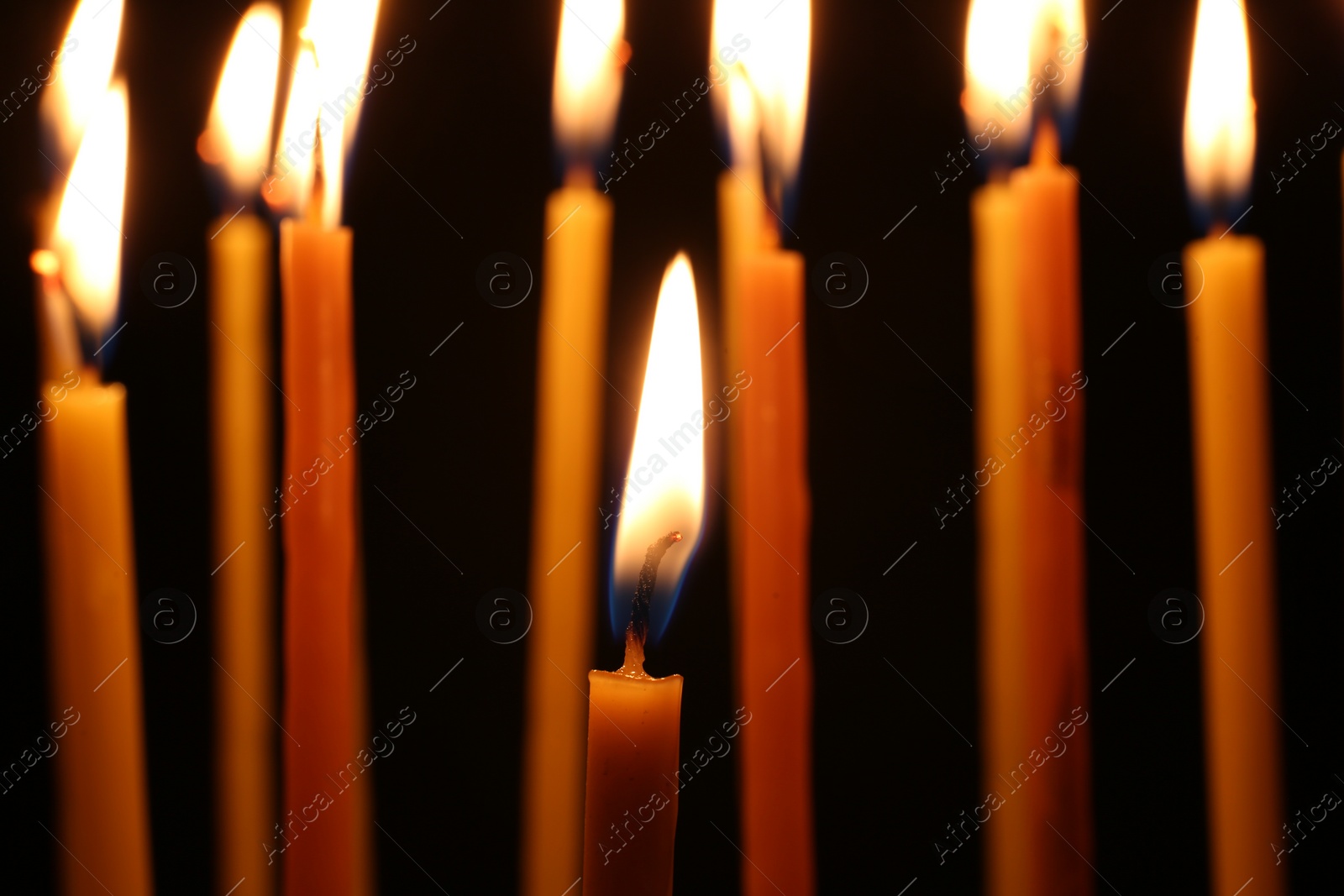 Photo of Many burning church candles on dark background, closeup