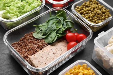 Photo of Glass and plastic containers with fresh food on black table, closeup