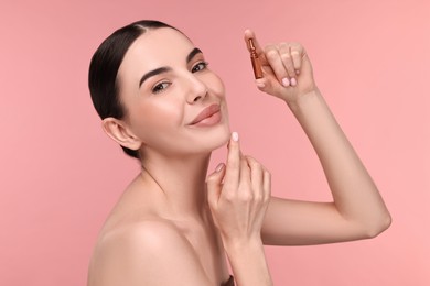 Photo of Beautiful young woman holding skincare ampoule on pink background