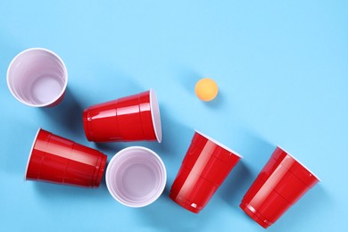 Photo of Plastic cups and ball on light blue background, flat lay. Beer pong game