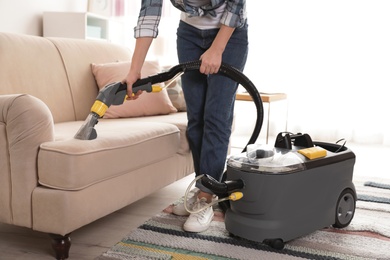 Photo of Woman removing dirt from sofa with vacuum cleaner at home, closeup