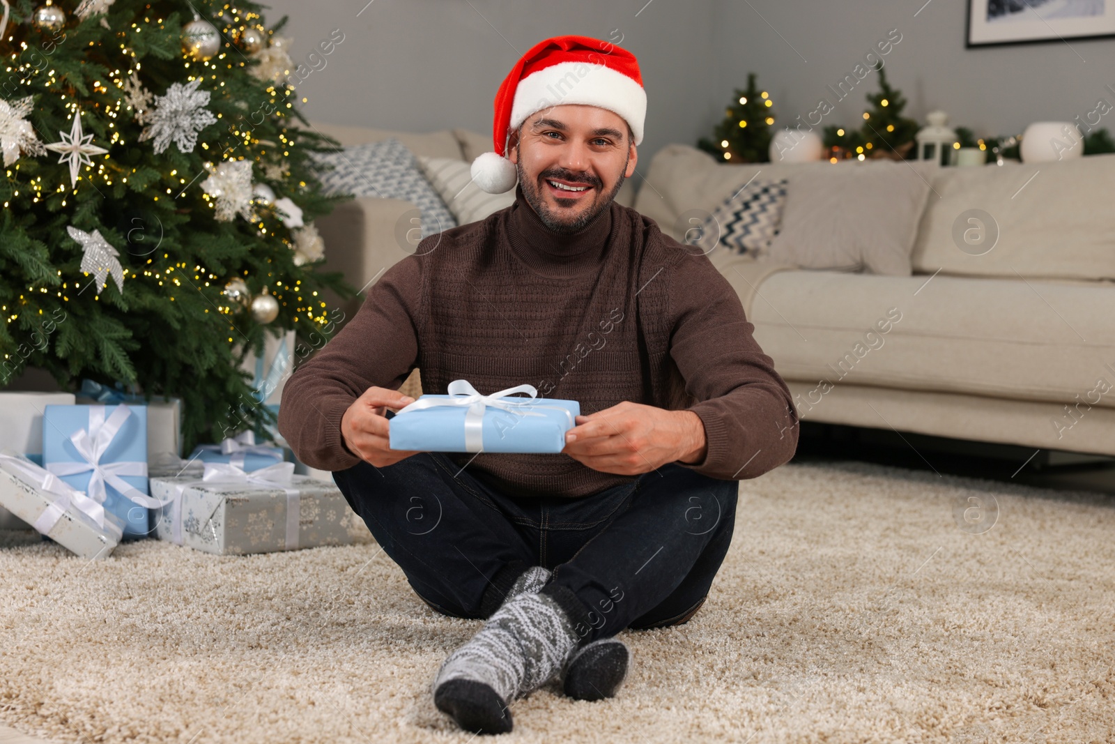 Photo of Happy man in Santa hat with Christmas gift at home