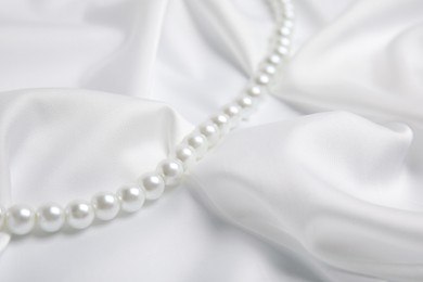 Photo of Beautiful pearls on white silk, closeup view