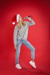 Photo of Happy woman in Santa Claus hat singing with microphone on red background. Christmas music