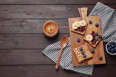 Different tasty toasts with nut butter and products on wooden table, flat lay. Space for text