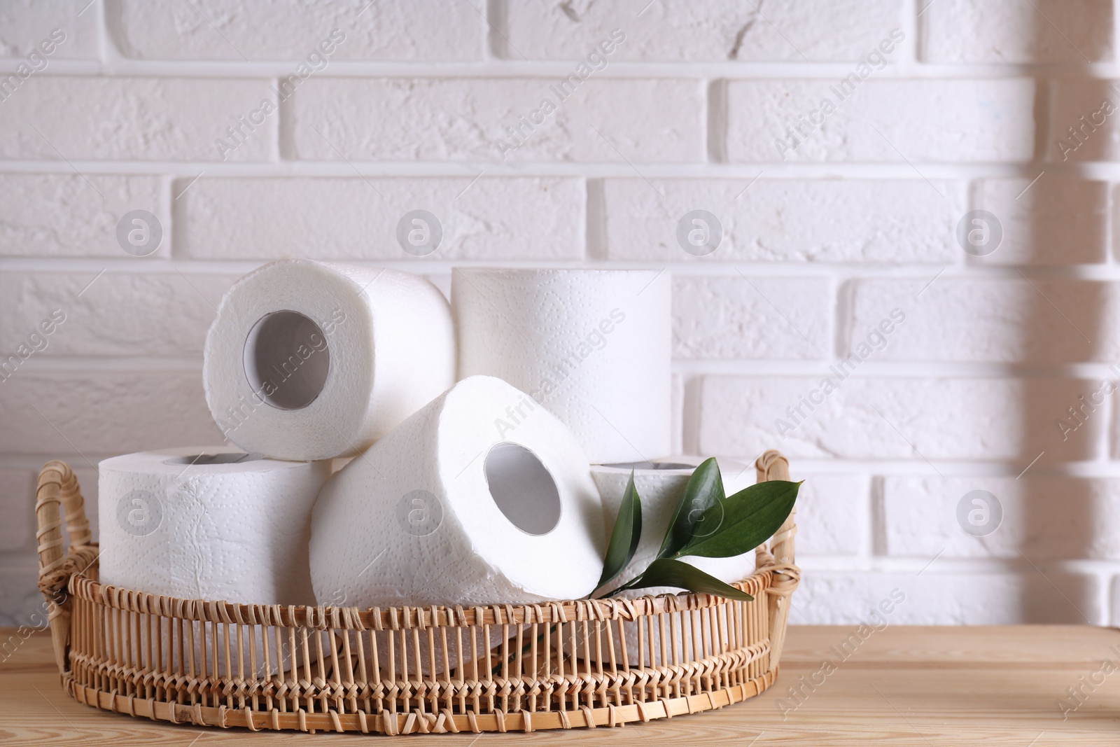 Photo of Toilet paper rolls and green leaves on wooden table near white brick wall