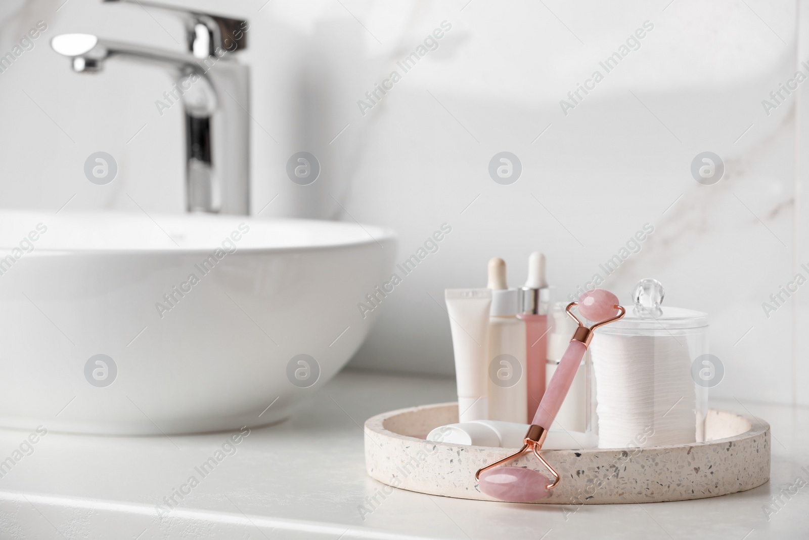 Photo of Natural face roller and tray with cosmetic products on counter in bathroom. Space for text