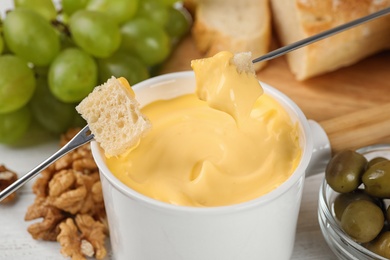 Dipping pieces of bread into tasty cheese fondue on table, closeup view