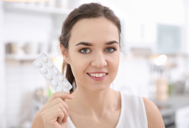 Photo of Young woman holding blister with vitamin pills indoors