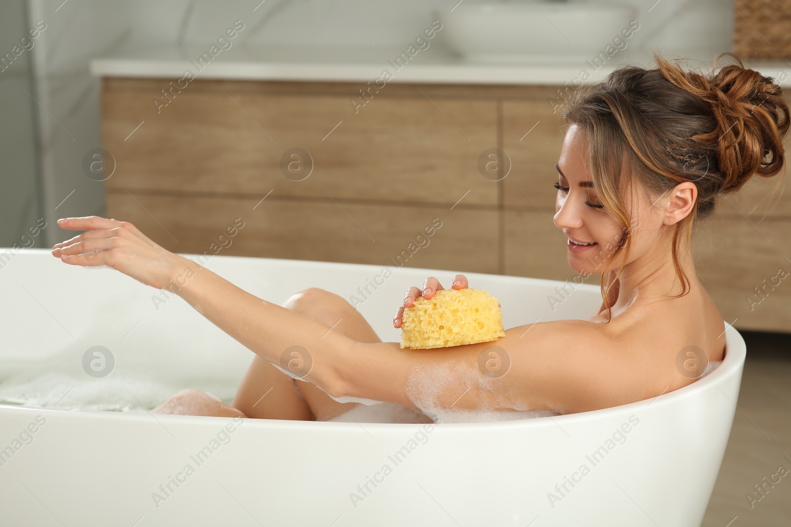 Photo of Beautiful woman with sponge taking bath indoors