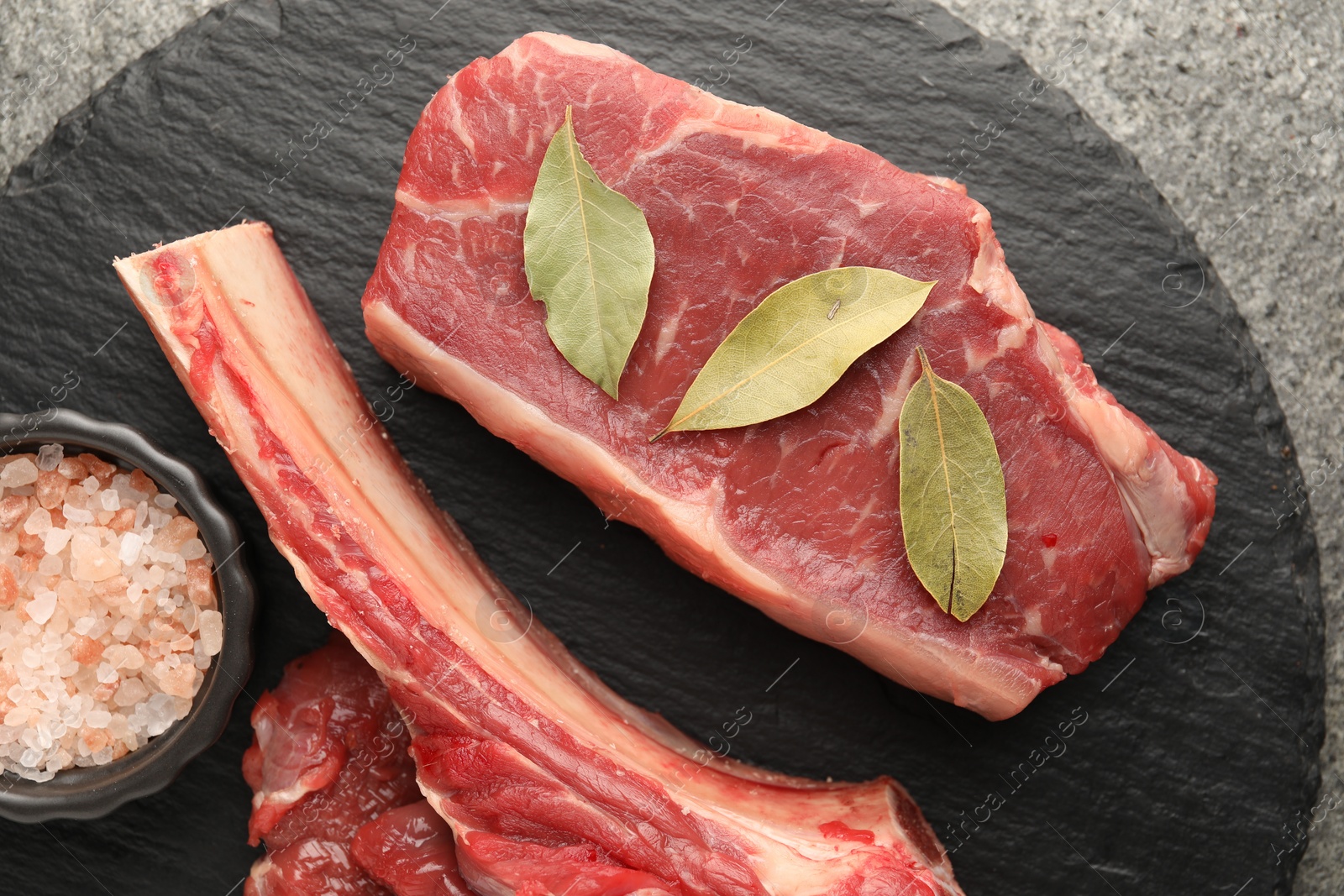 Photo of Pieces of raw beef meat and spices on grey table, top view