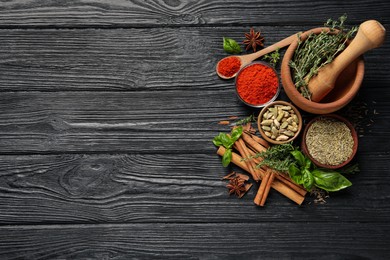 Different natural spices and herbs on black wooden table, flat lay. Space for text