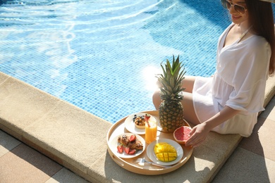 Young woman with delicious breakfast on tray near swimming pool, closeup. Space for text