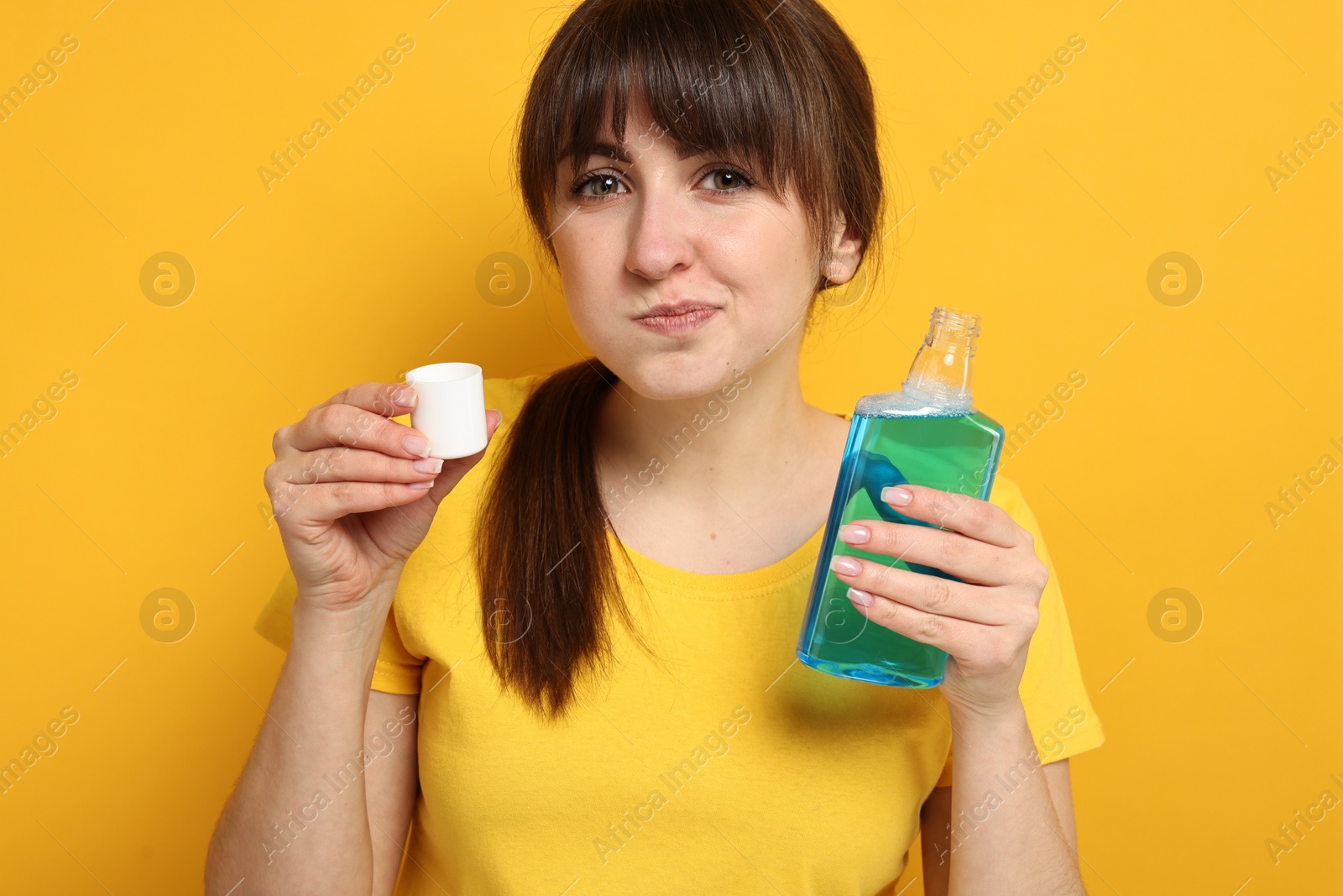 Photo of Young woman using mouthwash on yellow background