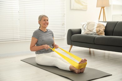 Photo of Senior woman doing exercise with fitness elastic band on mat at home