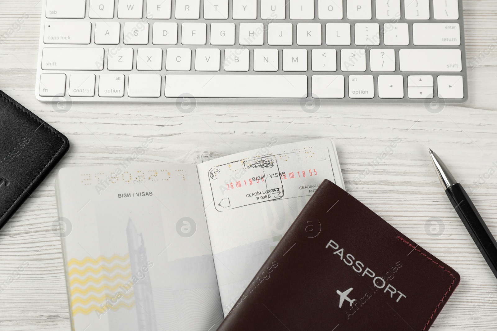 Photo of Moldova, Ceadir-Lunga - June 13, 2022: Passports with visa stamps, computer keyboard and pen on white wooden table, flat lay