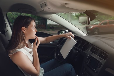 Photo of Stressed young woman with notebook talking on phone in driver's seat of modern car
