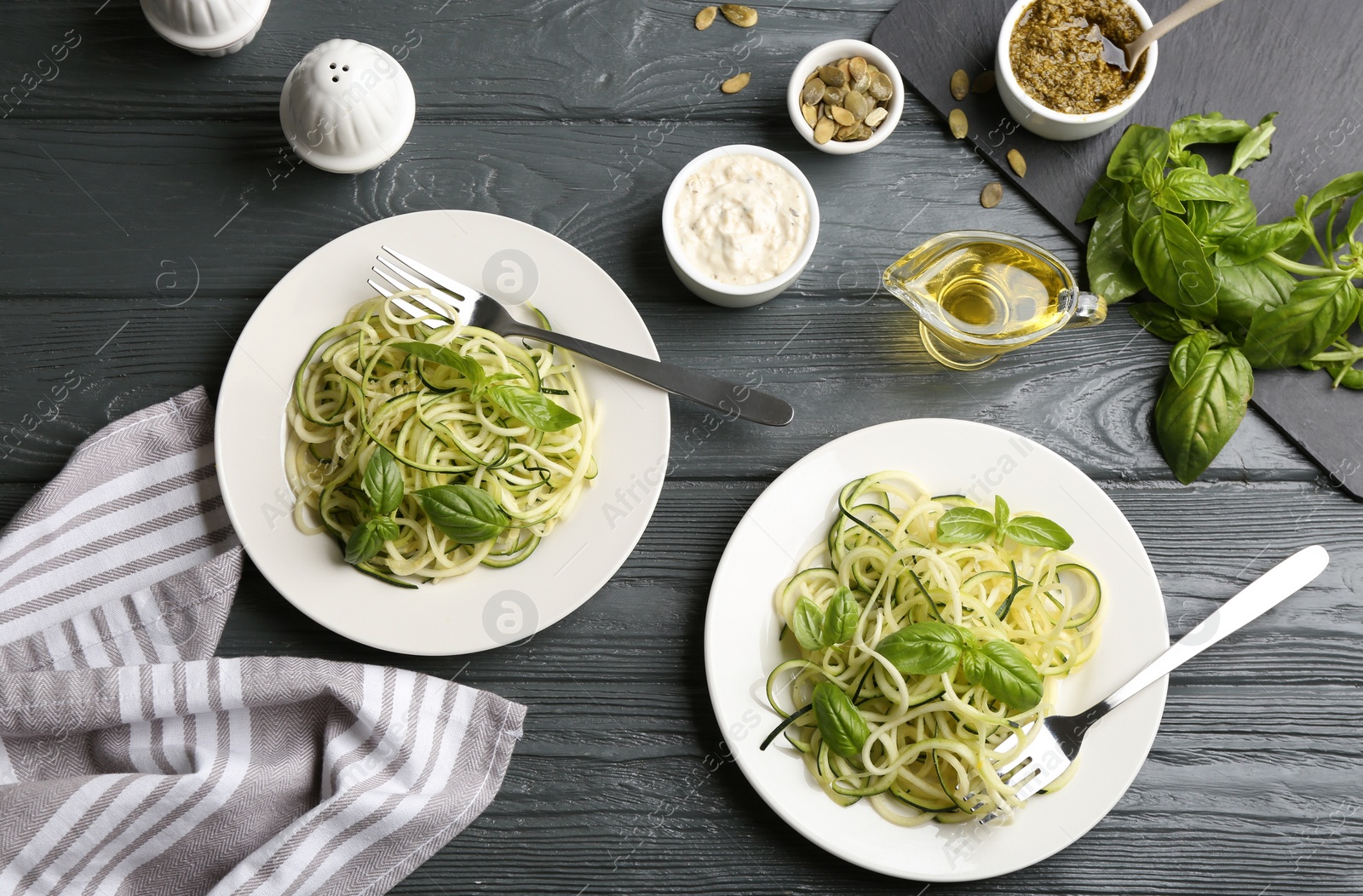 Photo of Delicious zucchini pasta with basil, pumpkin seeds and sauce served on grey wooden table, flat lay