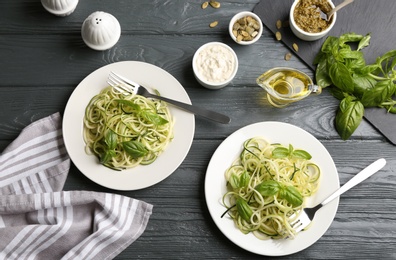 Delicious zucchini pasta with basil, pumpkin seeds and sauce served on grey wooden table, flat lay