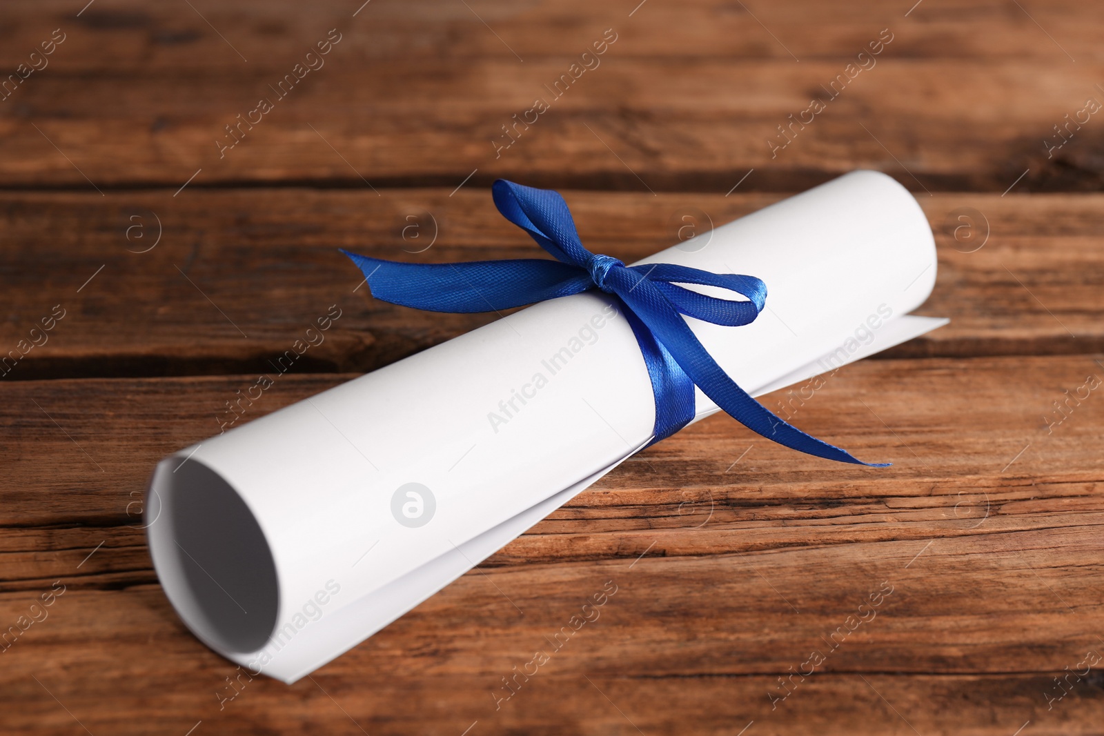 Photo of Rolled student's diploma with blue ribbon on wooden table