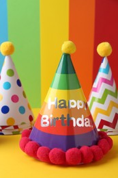 Different bright party hats with pompoms on color background, closeup