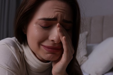 Photo of Sad young woman crying on bed at home, closeup. Loneliness concept